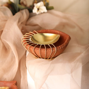 Gold plated metal diya encompassed by earthy terracotta with ornate wire detailing