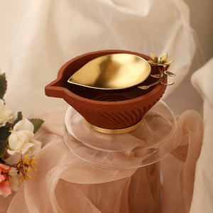 Gold plated metal diya encompassed by earthy terracotta with ornate floral detailing