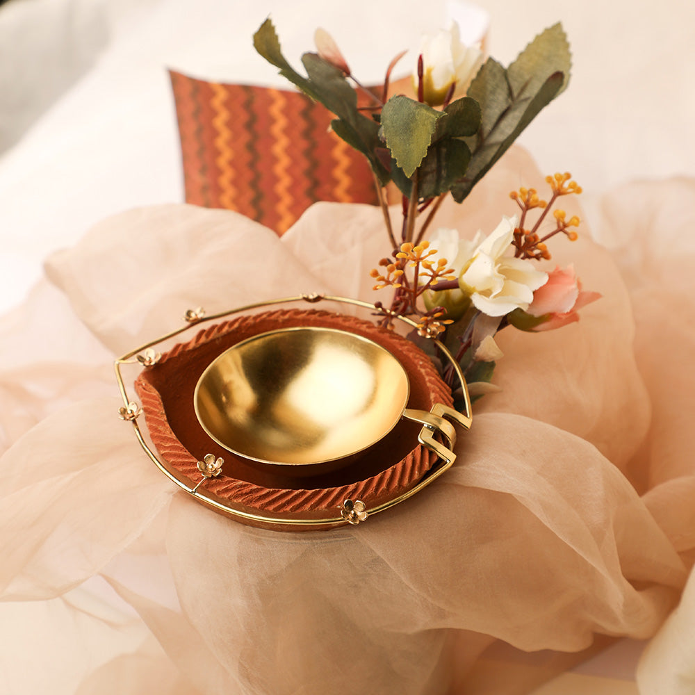 Gold plated metal diya encompassed by earthy terracotta with intricate floral border