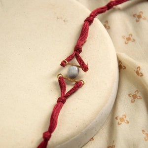 gold plated rakhi with a grey bead and maroon thread